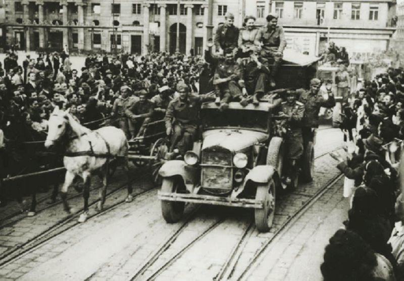 Zagreb, 9. svibnja 1945. godine. Kroz masu okupljenih građana iz Jurišićeve ulice na Trg pristiže kolona partizanskih kamiona i zaprežnih vozila s partizanima